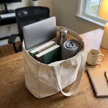 The tote packed with a laptop and books on a desk